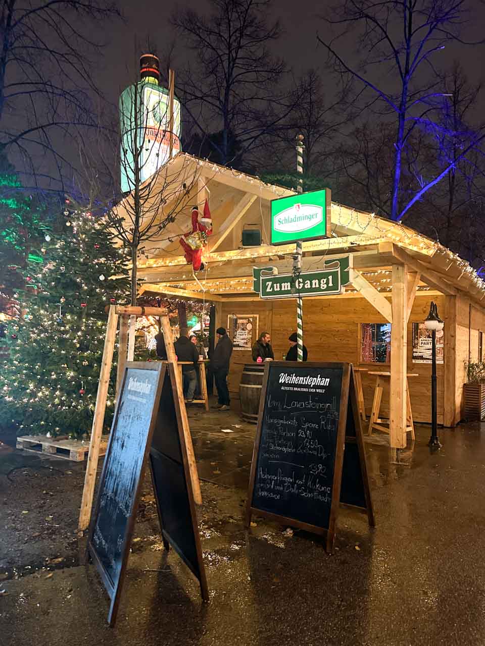 A wooden stall with festive lights, chalkboard menus, and a large Christmas tree at the University of Vienna Christmas Market