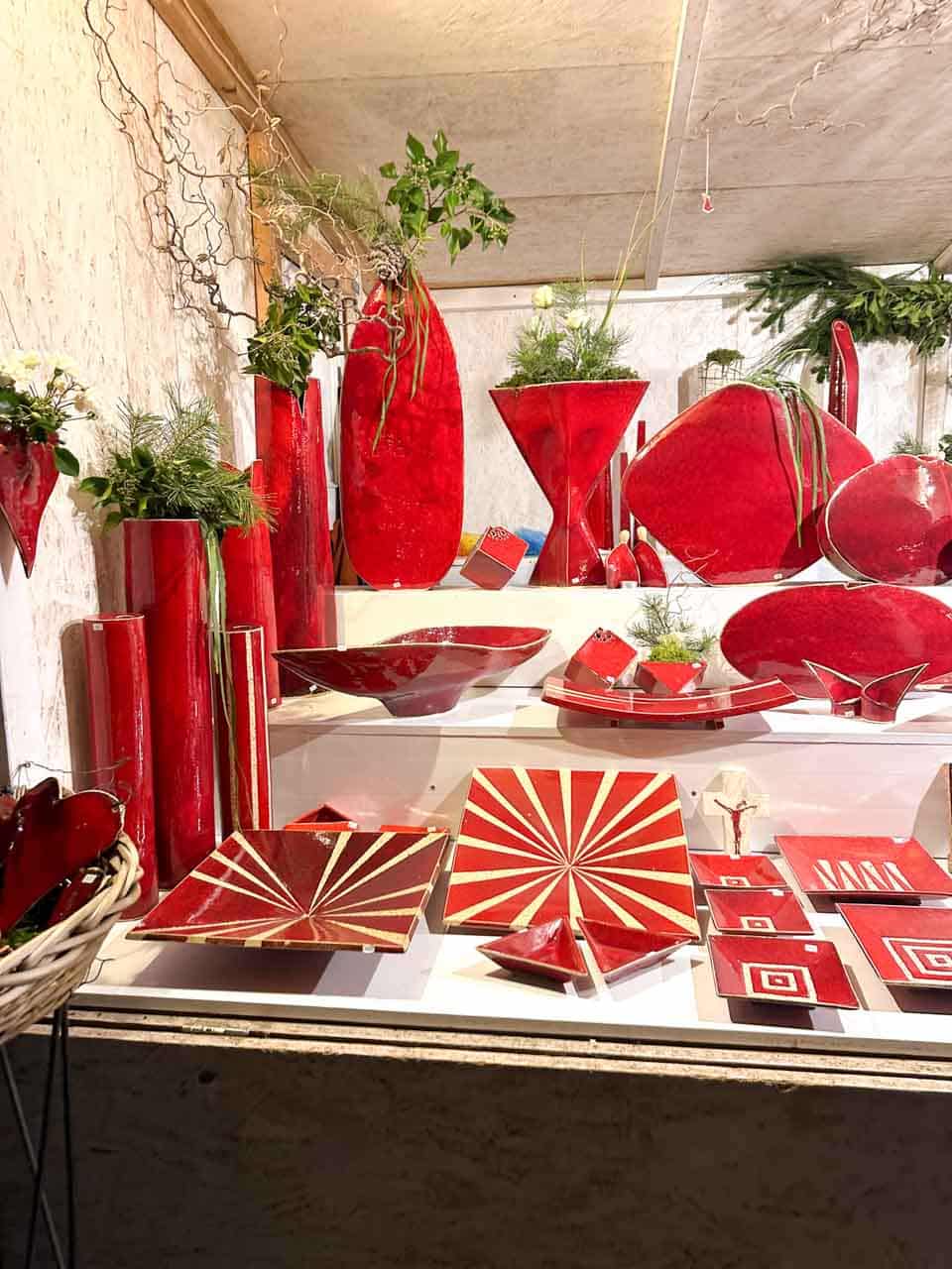 A market stall showcasing red ceramic vases, bowls, and plates at the Karlsplatz Christmas market in Vienna
