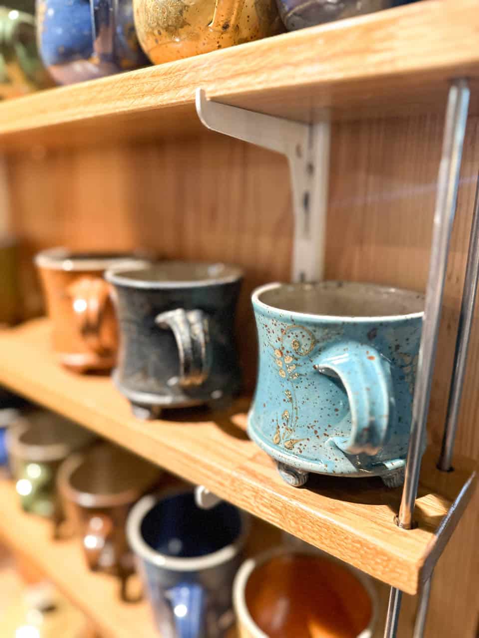 Handmade ceramic mugs in different colours displayed on wooden shelves at a Christmas market stall on Karlsplatz in Vienna
