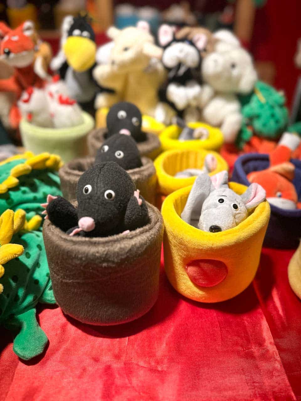 Soft toy moles and mice peeking out of colourful felt cups on a table covered with red fabric