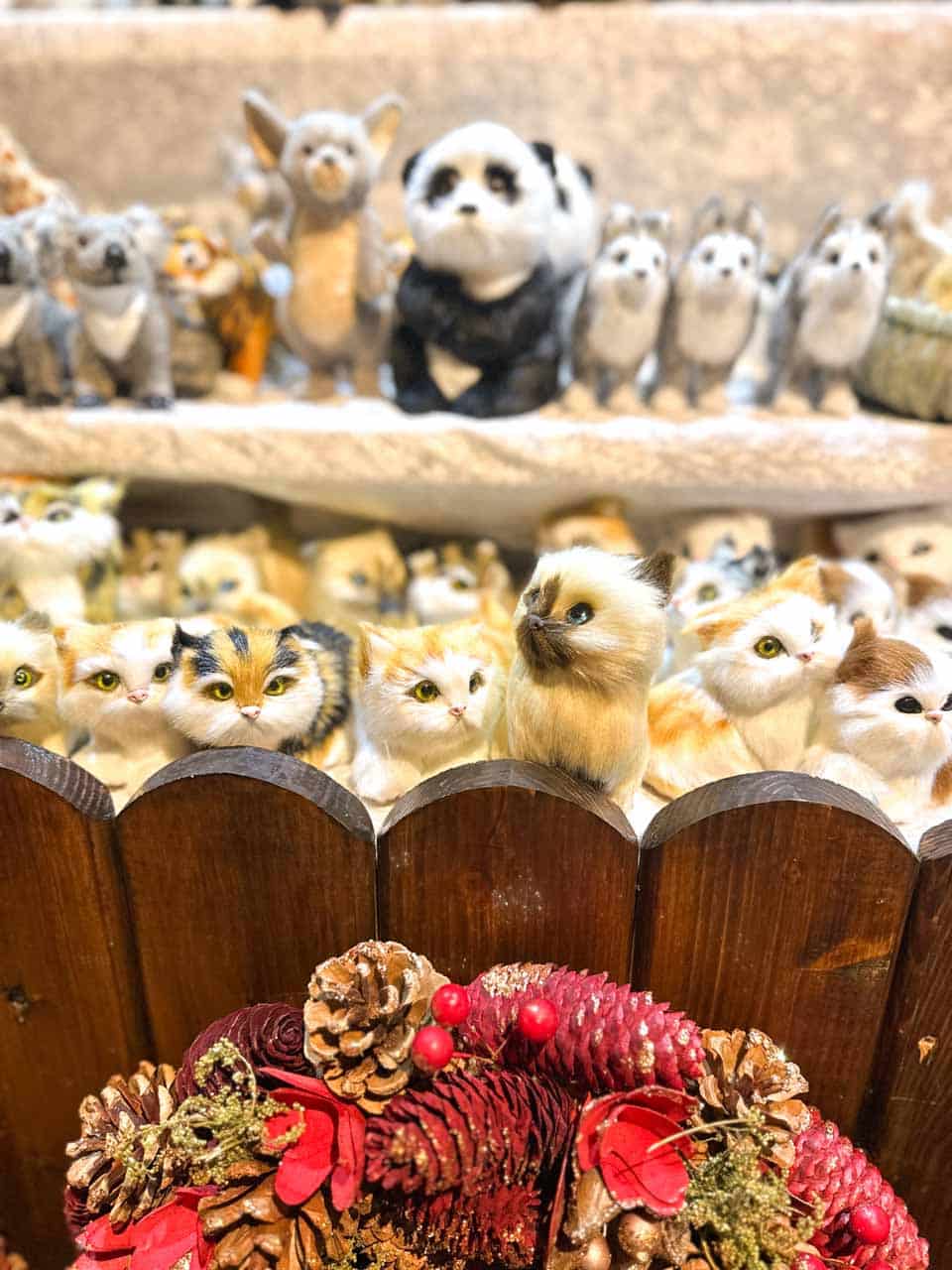 A display of stuffed animal toys, including pandas and cats, behind a festive wreath with red pinecones and berries