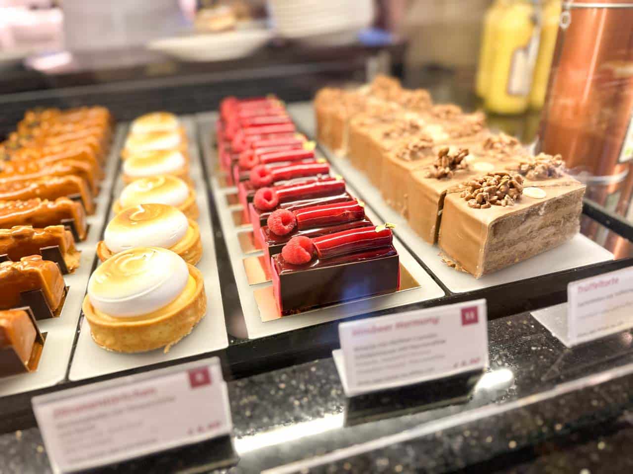 A glass display case filled with elegant pastries, including lemon tarts, raspberry slices, and nutty cakes at Café Central in Vienna, Austria