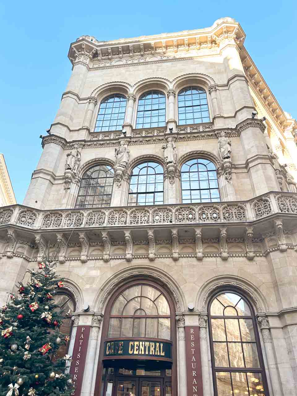 The grand exterior of Café Central in Vienna with a festive Christmas tree by the entrance