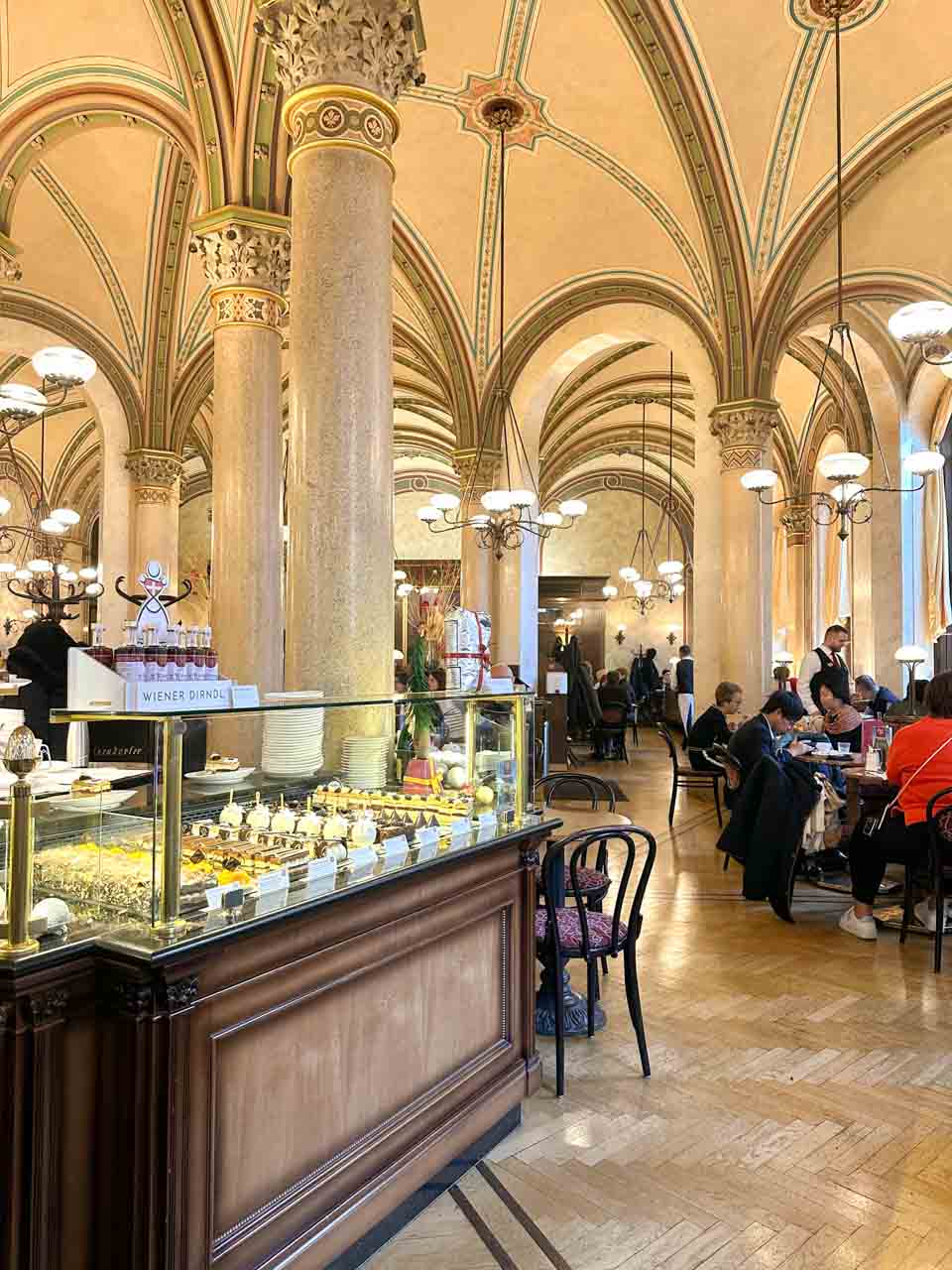 The interior of Café Central with high vaulted ceilings, marble columns, and a pastry counter filled with desserts