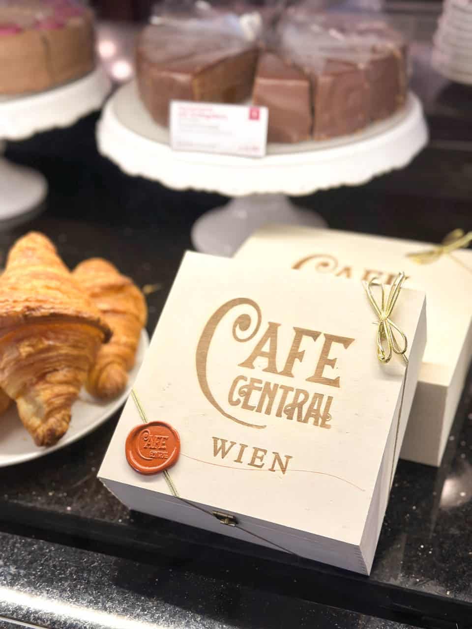 A gift box from Café Central with a wax seal, displayed alongside buttery croissants and a chocolate cake