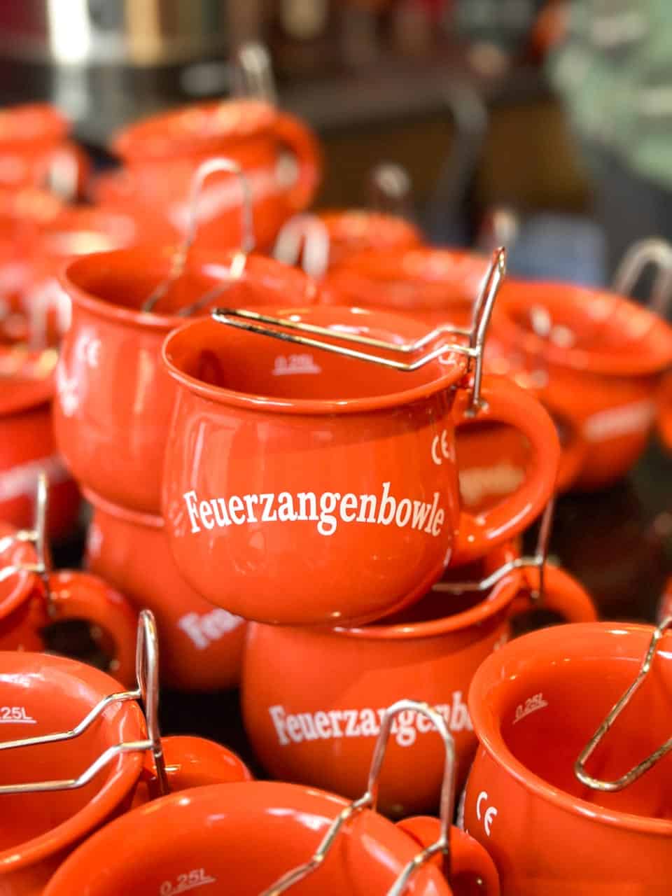 Bright red Feuerzangenbowle mugs with metal holders stacked neatly at a market stall at the Advent im Gartenpalais Liechtenstein Christmas market