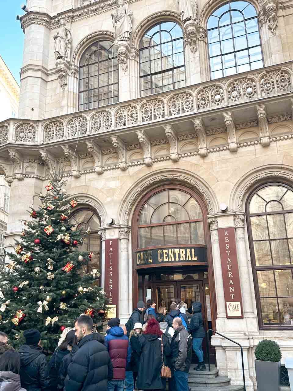 The front entrance of Café Central in Vienna with a towering Christmas tree and a crowd of people waiting outside