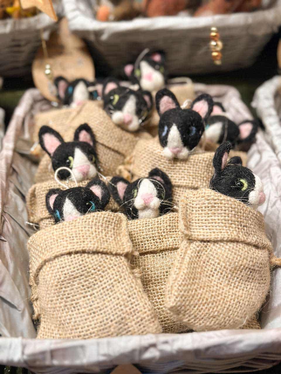 Handmade black and white felt mice tucked into small burlap sacks on display at a Christmas market stall in Vienna