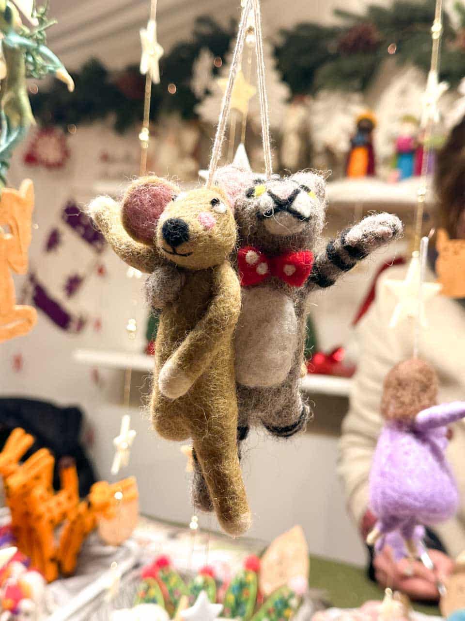 Woollen ornaments of a mouse and a cat hanging together, surrounded by festive decorations at a Christmas market stall in Vienna