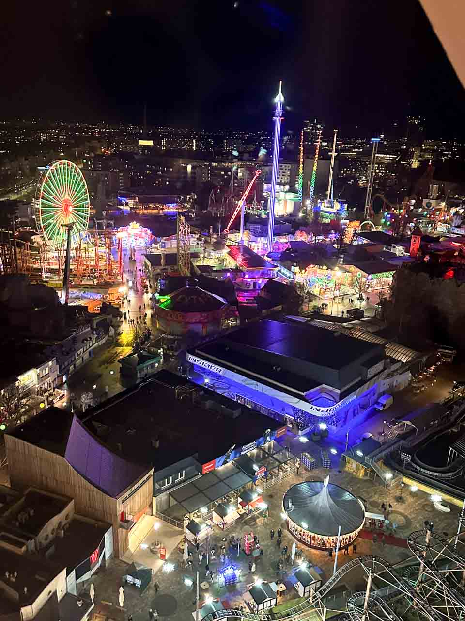 Aerial view of Vienna's Prater amusement park at night, with glowing rides, a Ferris wheel, and festive lights