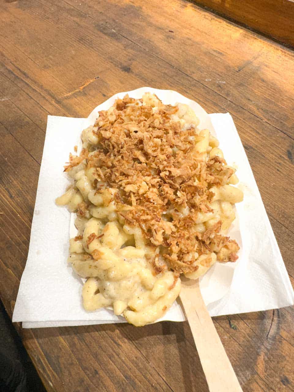 A paper plate of creamy cheese spaetzle topped with crispy fried onions at the Weihnachtsmarkt am Hof Christmas market in Vienna