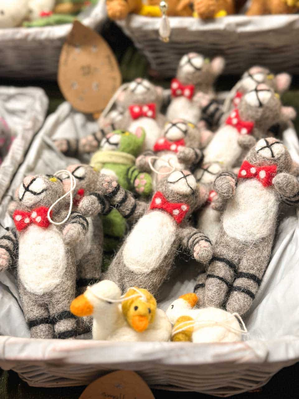 Handmade felt animal decorations, including mice in red bow ties and ducks, displayed in a woven basket at a market stall in Vienna