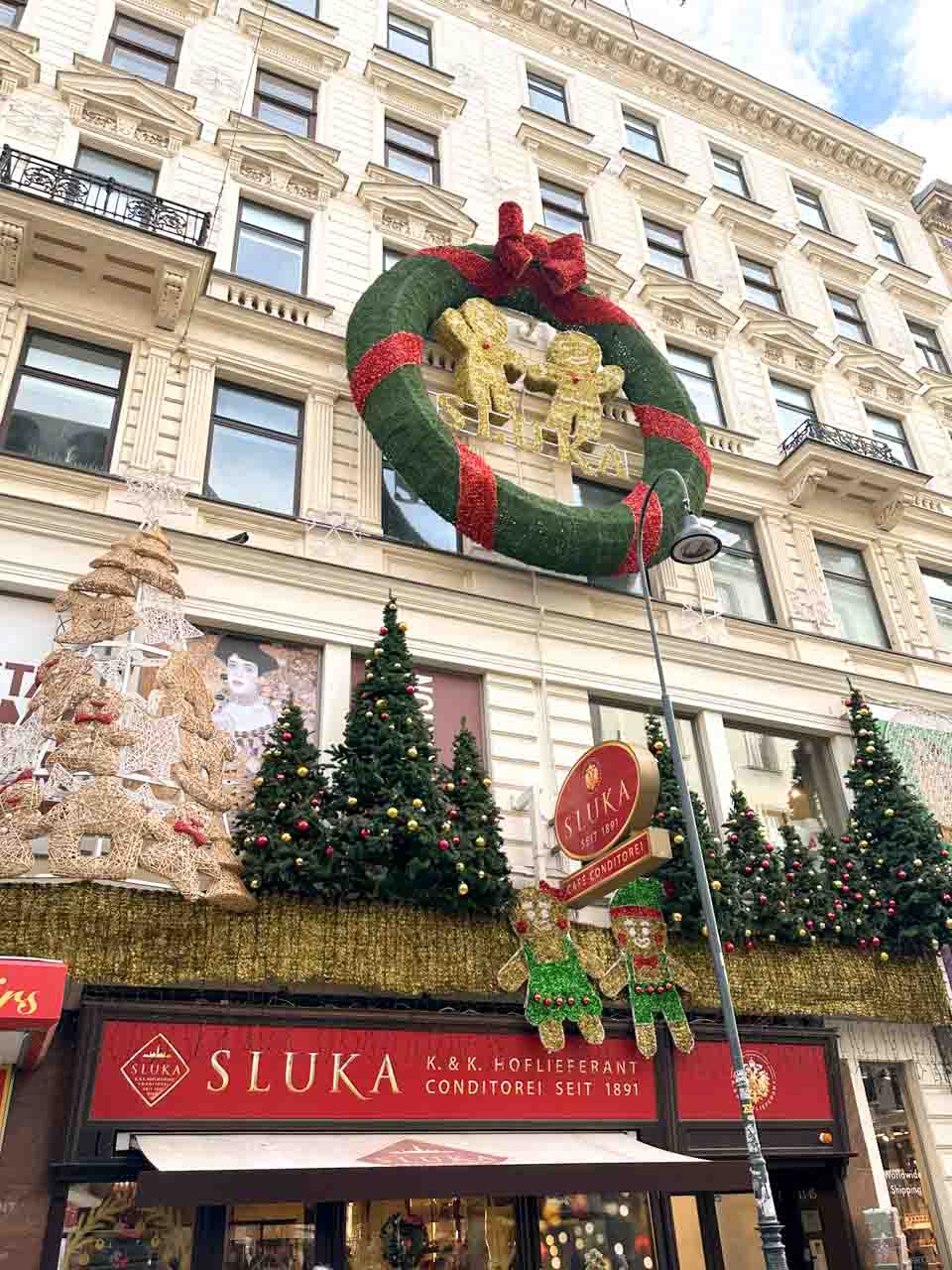 A café façade decorated with Christmas trees, a giant festive wreath, and gingerbread figures in Vienna