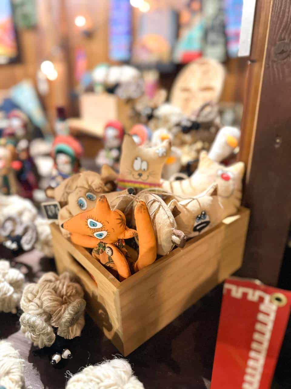 A wooden box filled with handmade fabric toys, including a fox and cat, displayed on a Christmas market stall