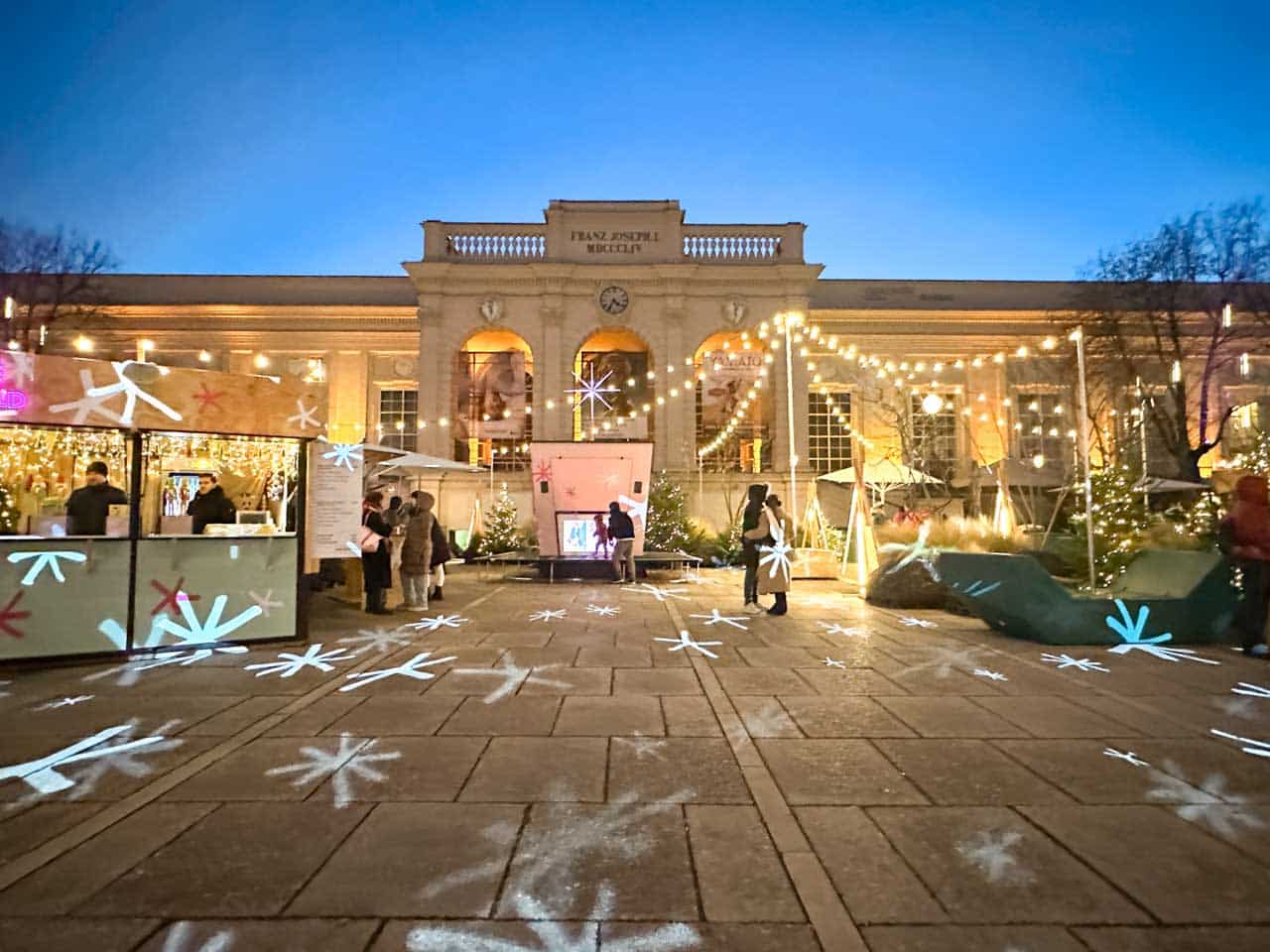 Winter in MQ Christmas market in Vienna, with illuminated stalls and snowflake-shaped light projections on the ground
