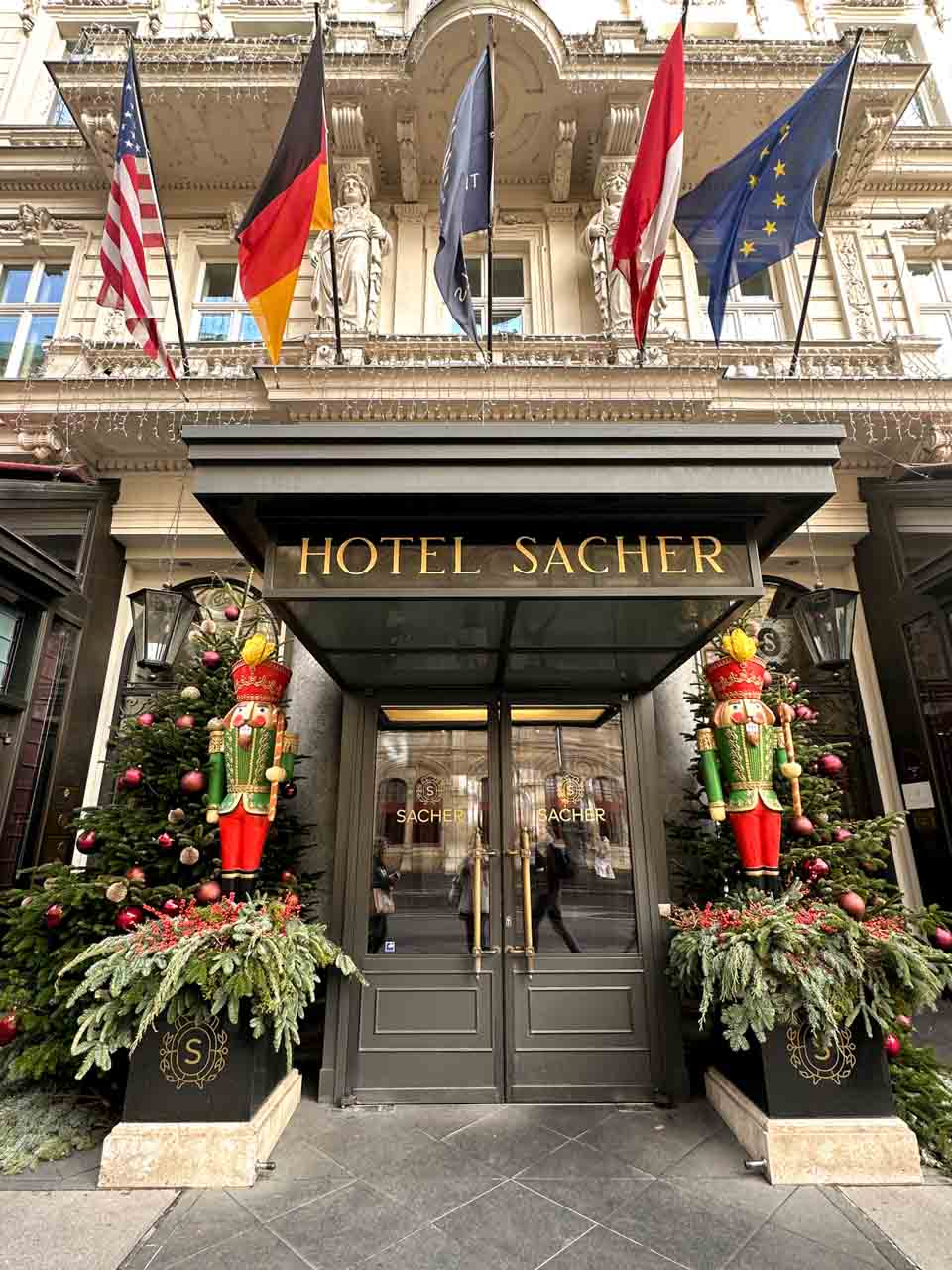 The entrance of Hotel Sacher in Vienna, adorned with nutcracker figures, Christmas trees, and festive decorations on either side