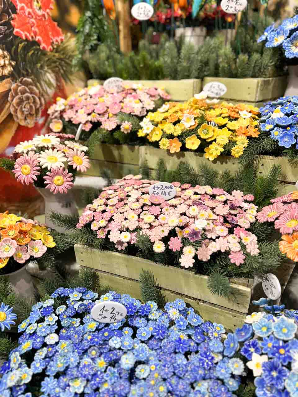 Bright ceramic flowers in shades of pink, yellow, and blue displayed in pots and wooden crates at the Christmas market on Maria-Theresien-Platz in Vienna