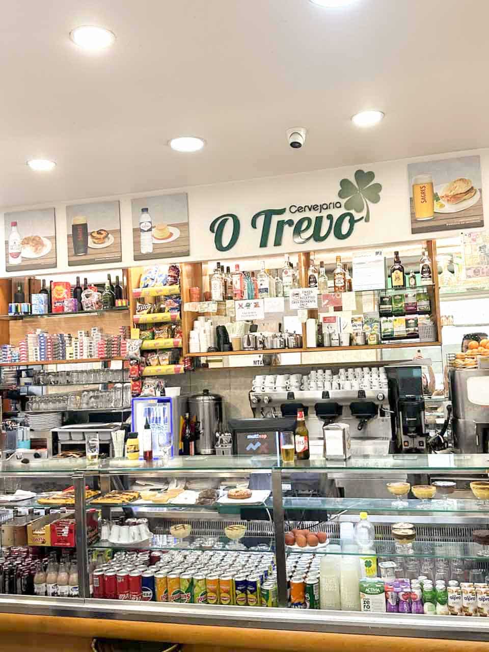 The counter inside O Trevo, lined with drinks, pastries, and food