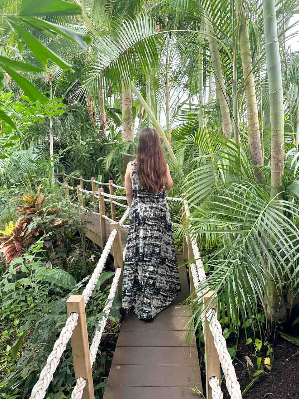A woman in a long dress walking on a wooden bridge through lush green tropical plants at the Lisbon Oceanarium