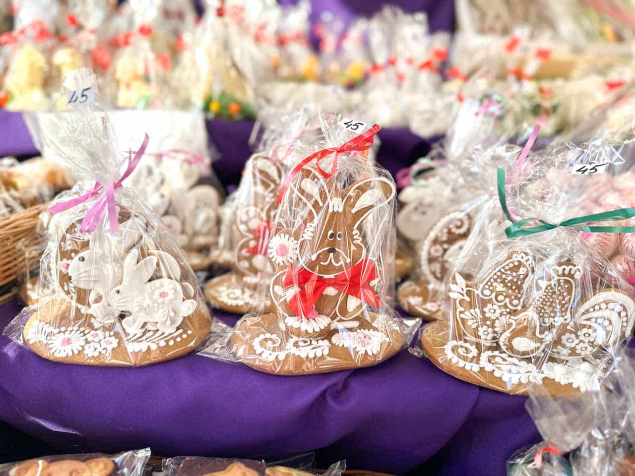 A close-up of iced gingerbread bunnies and chicks in clear gift bags, displayed on a purple cloth at the Katowice Easter Market