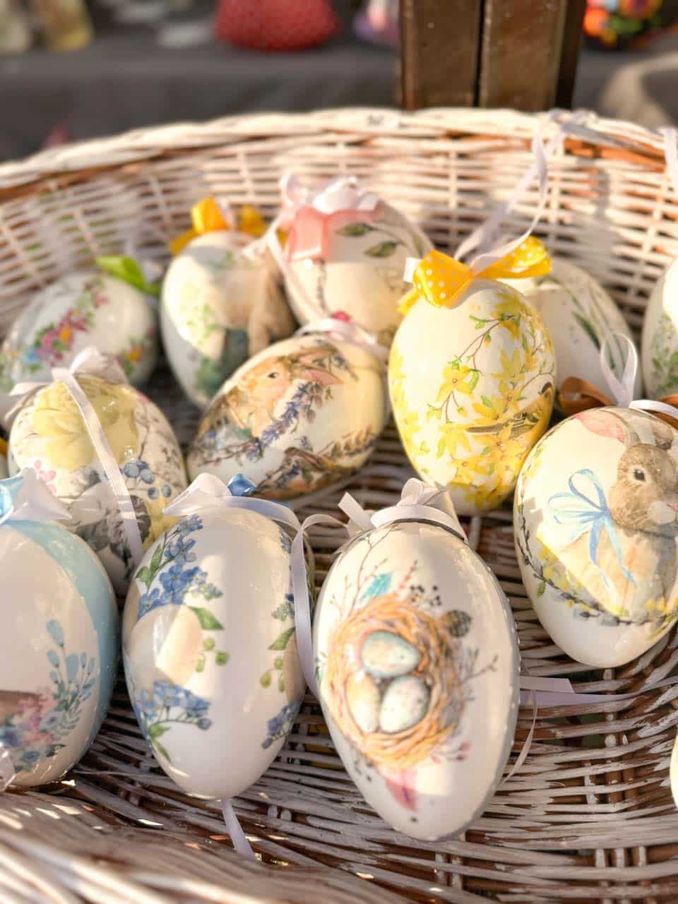 A basket of ceramic Easter eggs with painted flowers, birds, and bunnies, each tied with a pastel ribbon
