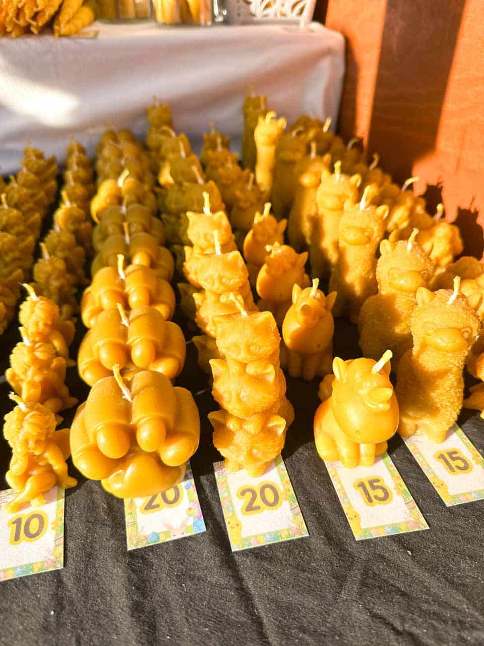 Rows of beeswax candles shaped like animals and pumpkins, lined up on a stall with price tags