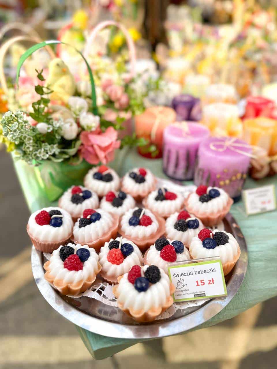 Cupcake-shaped candles topped with fake berries, displayed on a tray beside colourful Easter candles at the Katowice Easter Market