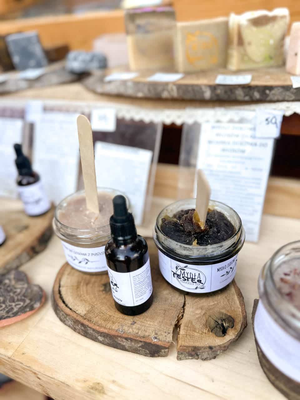 Jars of natural soap paste and oils on display, set on rustic wooden slices with handwritten labels at the Katowice Easter Market