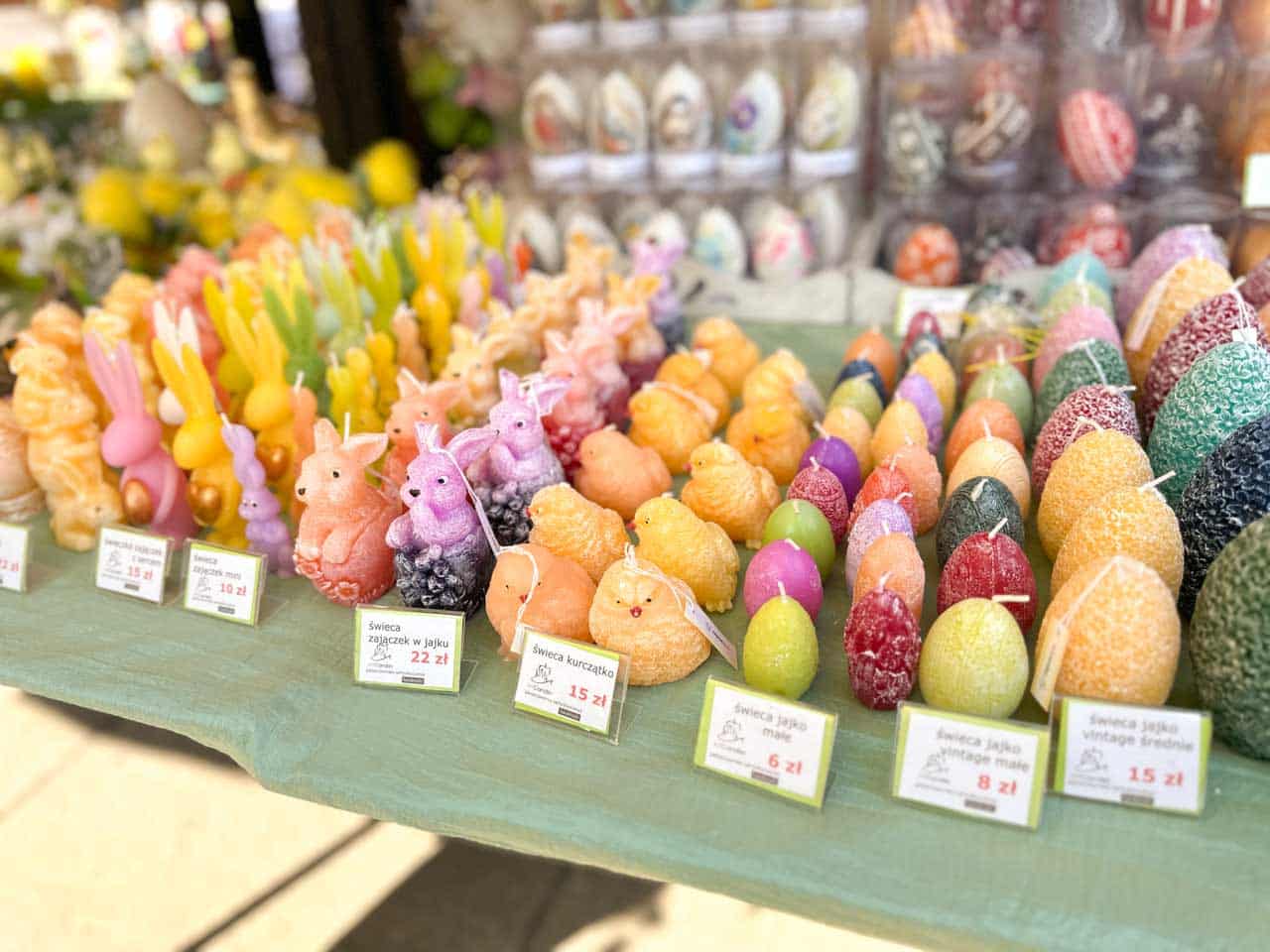 Rows of bunny, chick, and egg-shaped candles in pastel colours displayed on a green tablecloth