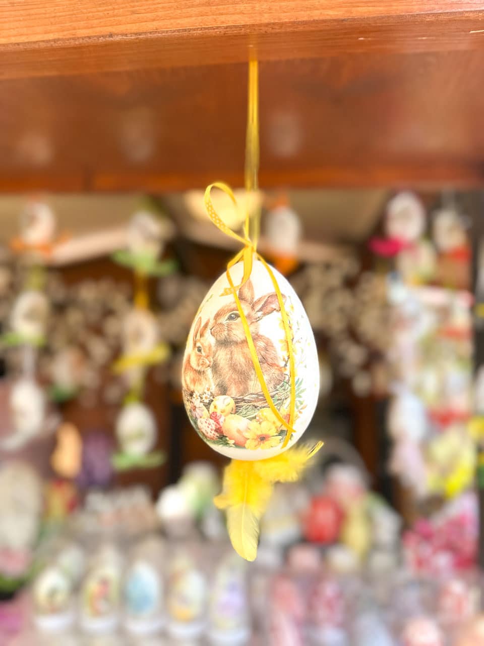 A close-up of a hanging Easter egg ornament with a rabbit design, tied with yellow ribbon and feather