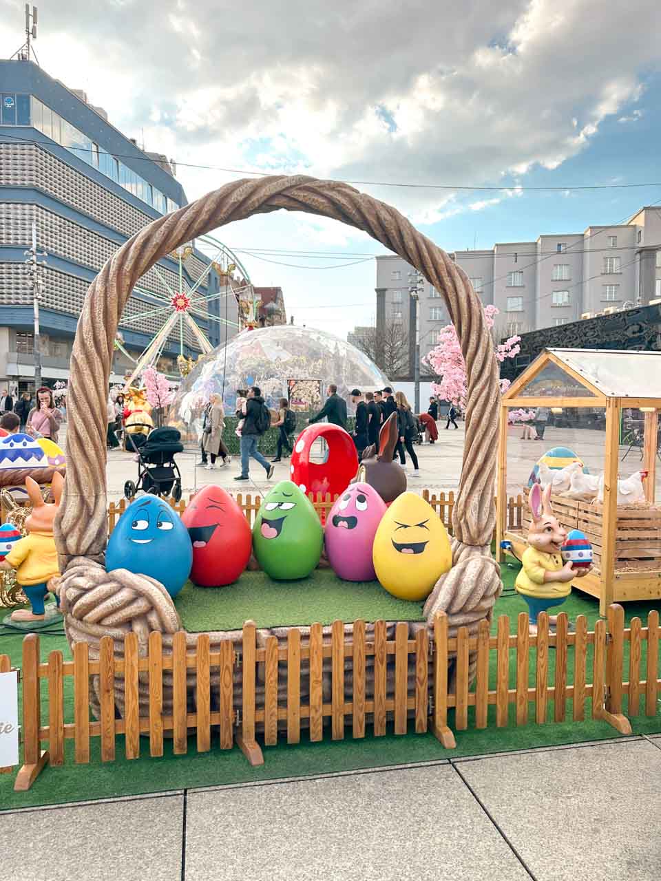 Colourful egg characters with funny faces inside a giant basket photo spot, surrounded by a picket fence, in the Market Square in Katowice, Poland