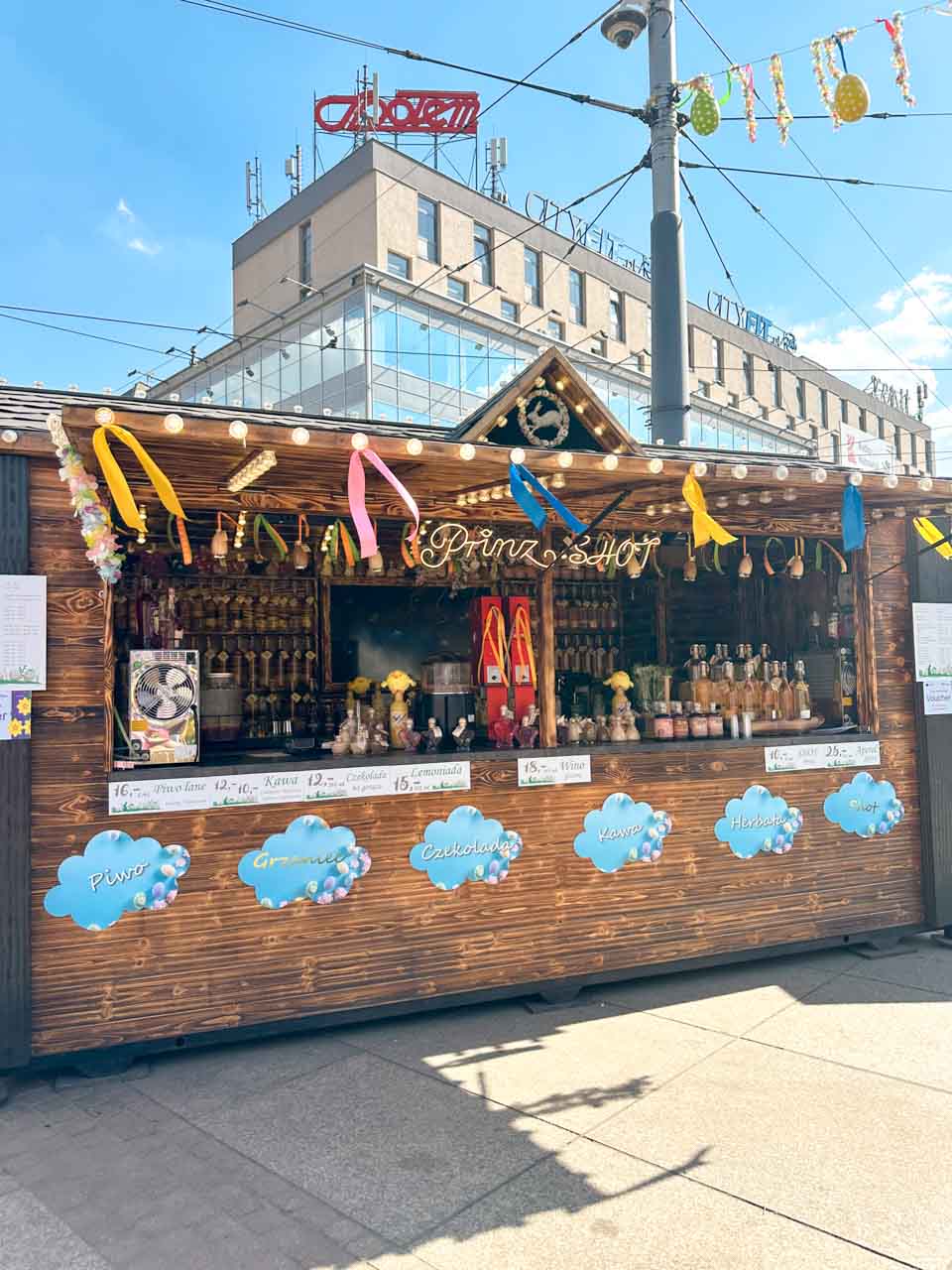 A wooden market stall decorated with Easter ribbons, selling drinks like beer, coffee, and mulled wine at the Katowice Easter Market