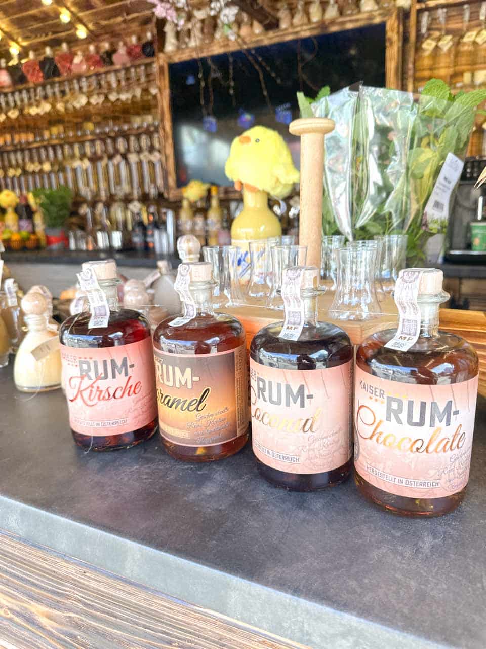 Four flavoured rum bottles lined up on a market stall counter with small shot glasses and Easter decorations in the background