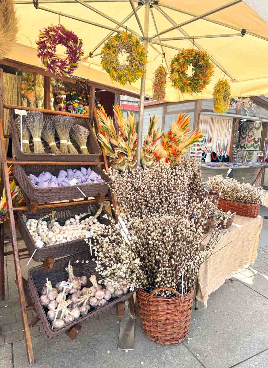 A colourful Easter stall with dried lavender, garlic, pussy willow branches, and hanging floral wreaths under a yellow canopy