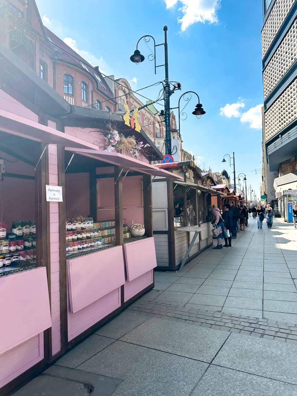 A row of pastel-coloured market stalls along a cobbled street, selling Easter goods with people browsing in the distance