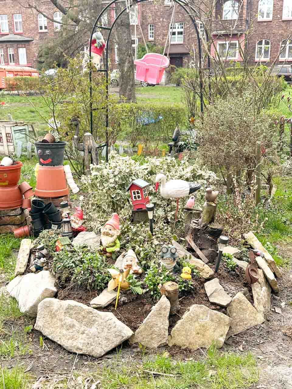 A small garden corner with gnomes, animal figures, and a pink toy swing hanging from a metal arch