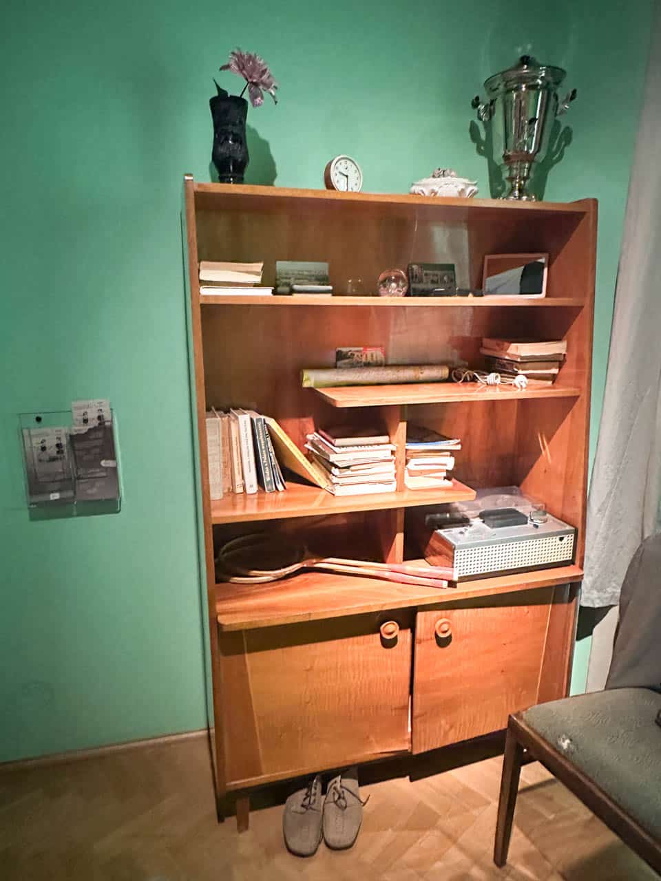 A wooden vintage bookcase filled with old books, a record player, and small personal items, in a room with green walls inside the Silesian Museum in Katowice