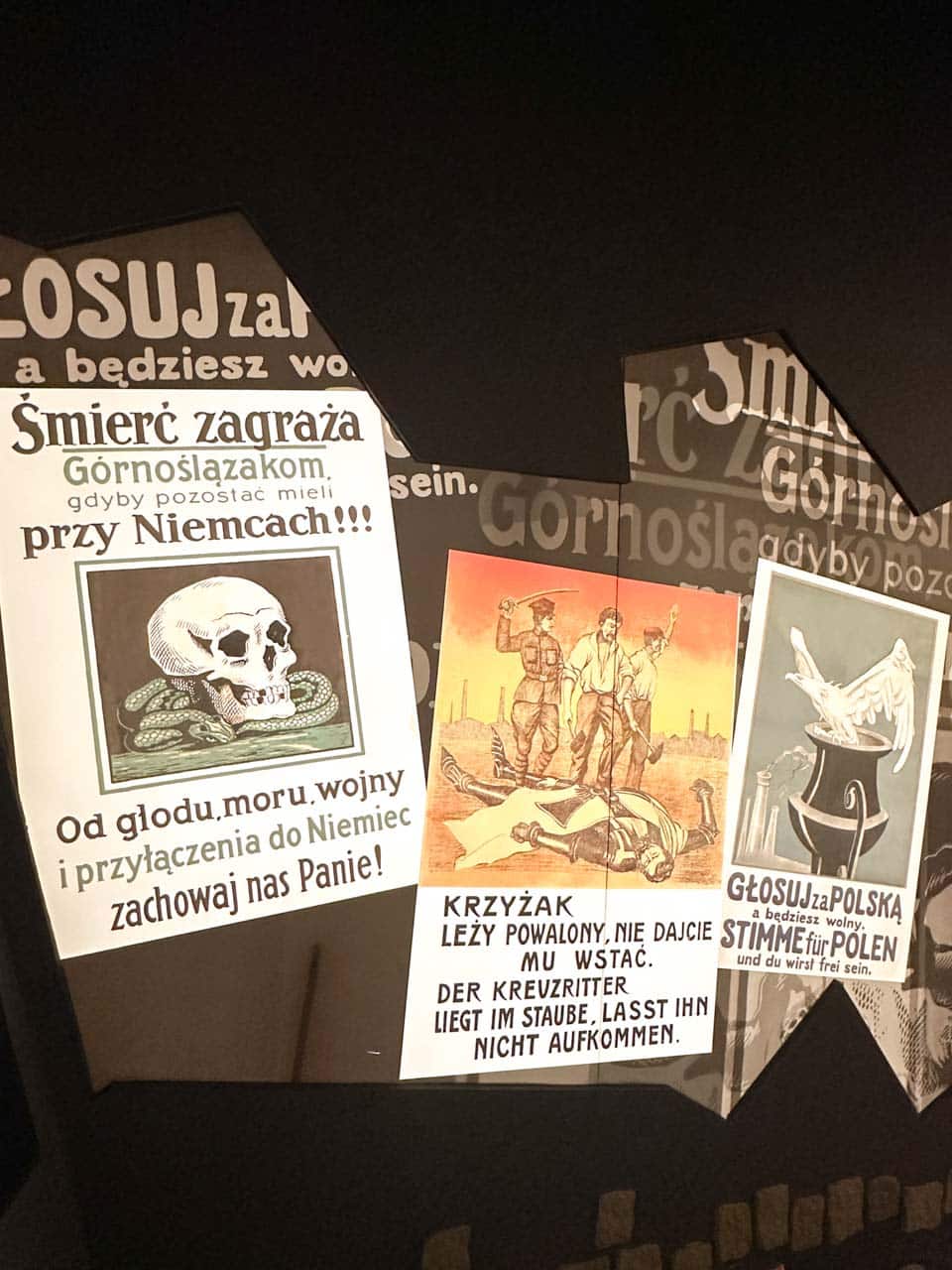 Close-up of three dramatic propaganda posters warning Upper Silesians about German threats, displayed in a dark space at the Silesian Museum in Katowice