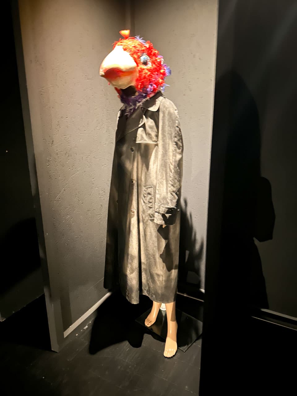 A mannequin wearing a long coat with a colourful bird mask in a dark, spotlighted corner at the Silesian Museum in Katowice