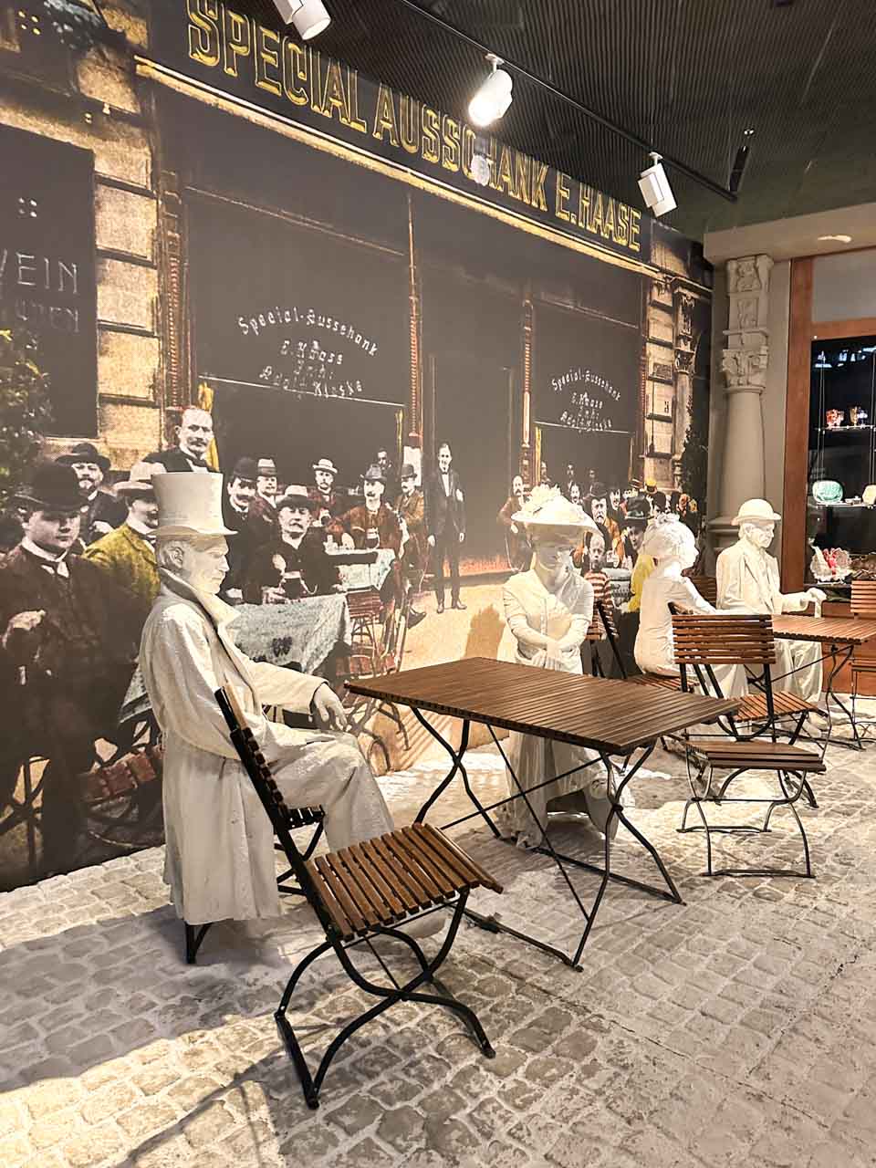 Lifelike statues in old-fashioned clothes sitting at caf&eacute; tables in front of a large vintage street photo inside the Silesian Museum in Katowice, Poland