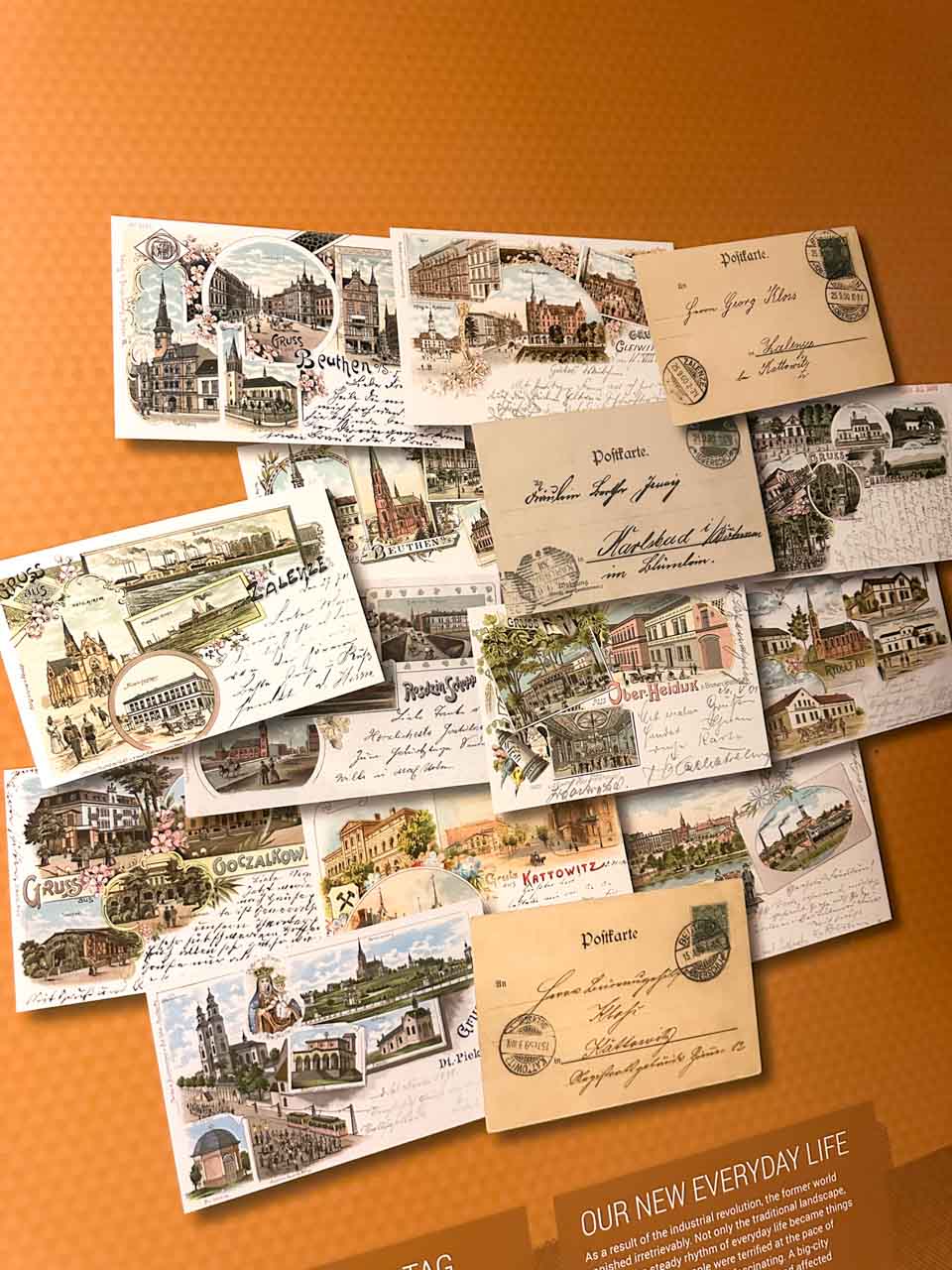 A collage of old postcards showing views of Katowice and nearby cities, displayed on an orange background inside the Silesian Museum in Katowice, Poland