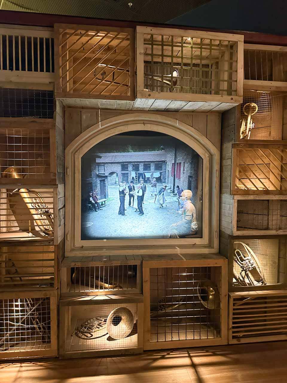 A screen showing a black-and-white scene surrounded by wooden crates holding old musical instruments