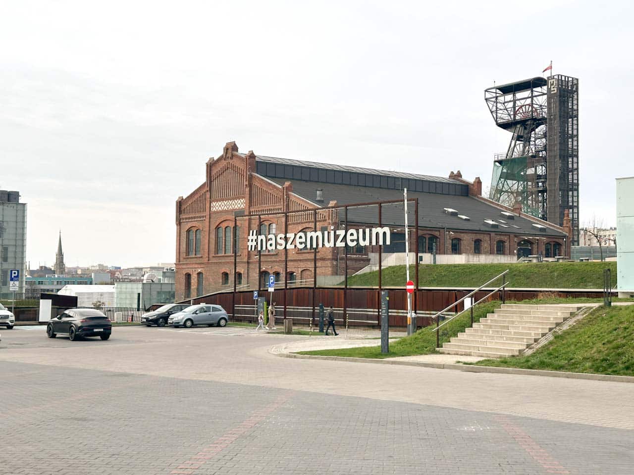 A red-brick building of the Silesian Museum in Katowice, Poland with a mining tower behind it and a large #naszemuzeum sign out front