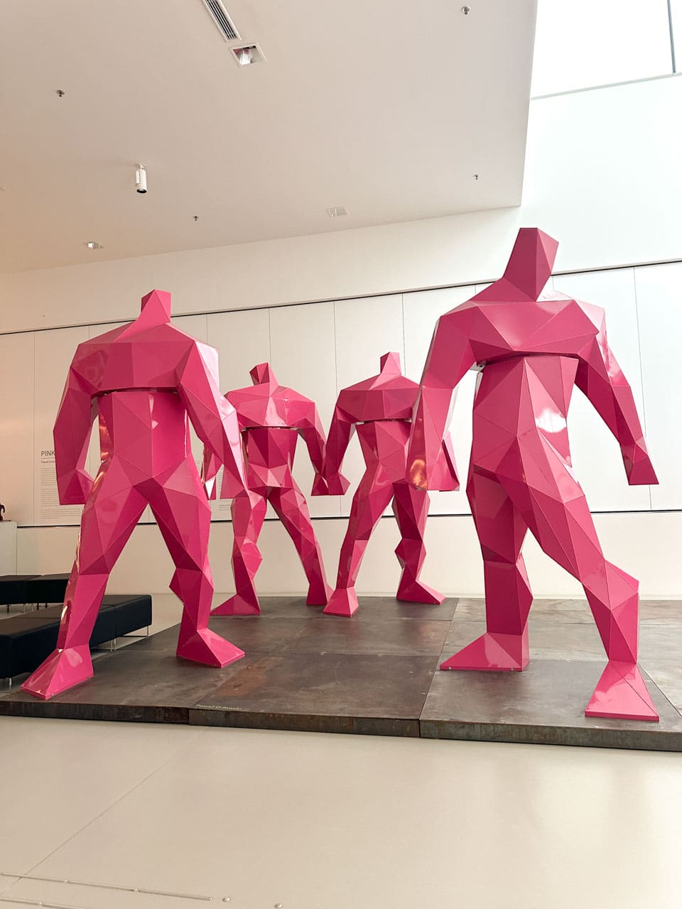 A group of five large pink geometric statues of human figures standing in a circle inside the Silesian Museum in Katowice