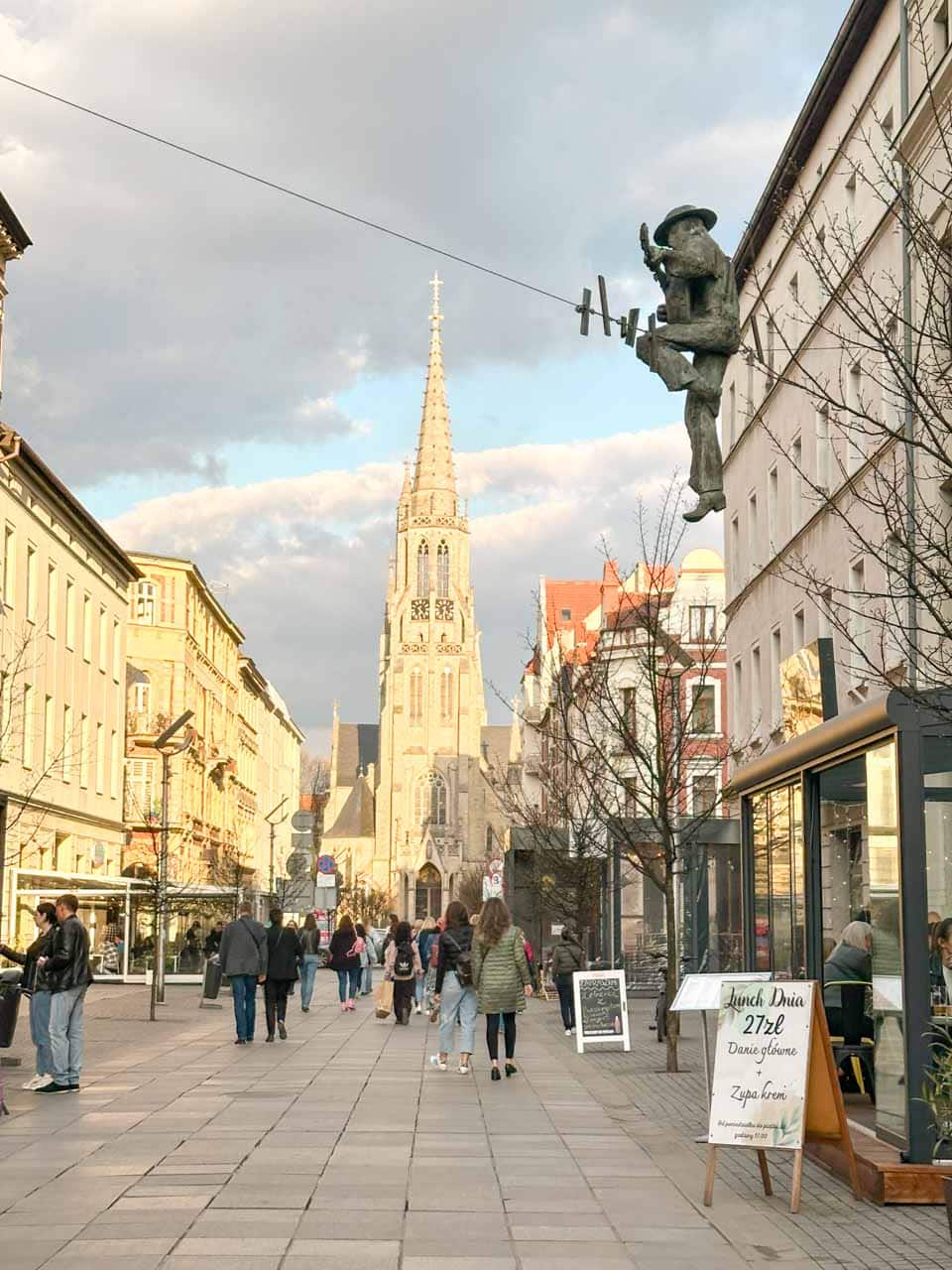 Mariacka Street in Katowice with people walking towards a church, under a sculpture of a man balancing on a wire