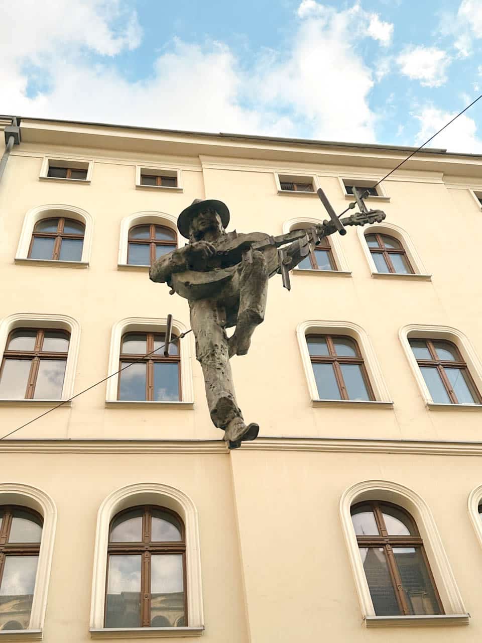 Sculpture of a man with a hat playing guitar, balancing on a wire above Mariacka street in Katowice