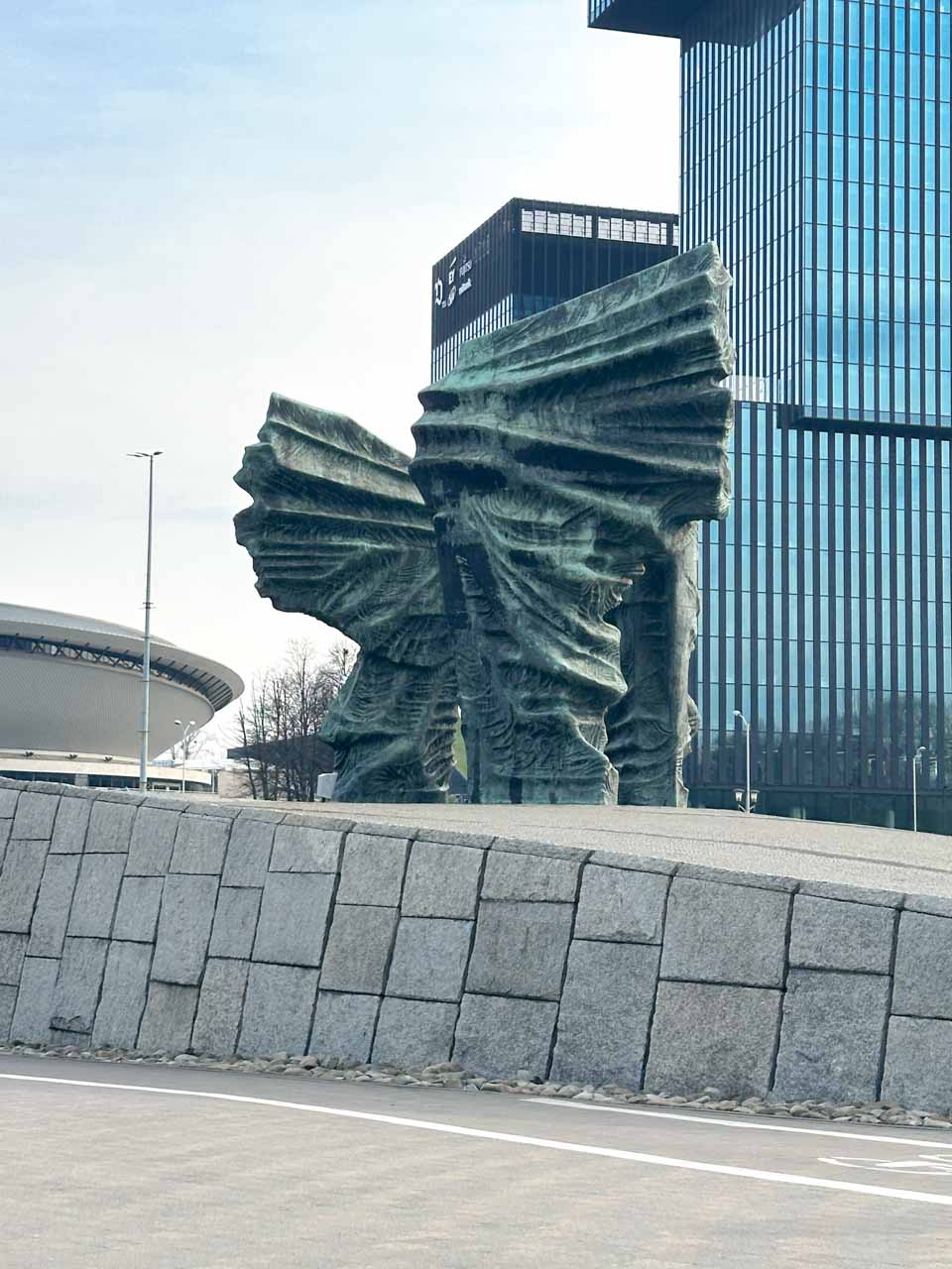 Silesian Insurgents' Monument in Katowice, Poland with three wing-like forms in front of modern glass buildings