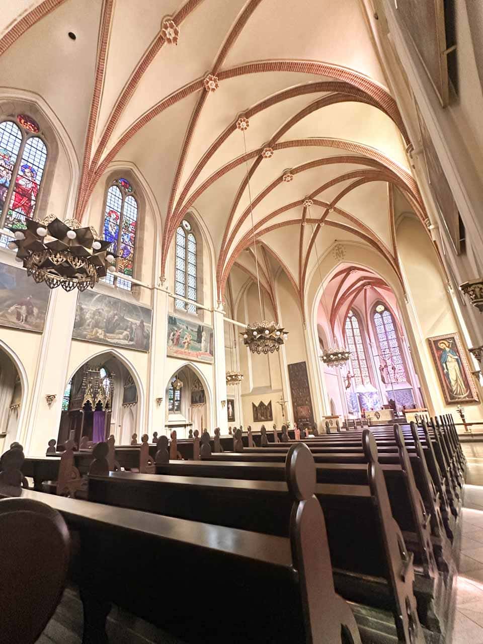 Rows of dark wooden pews inside the Immaculate Conception of the Blessed Virgin Mary Church in Katowice, with tall stained glass windows and vaulted ceilings above