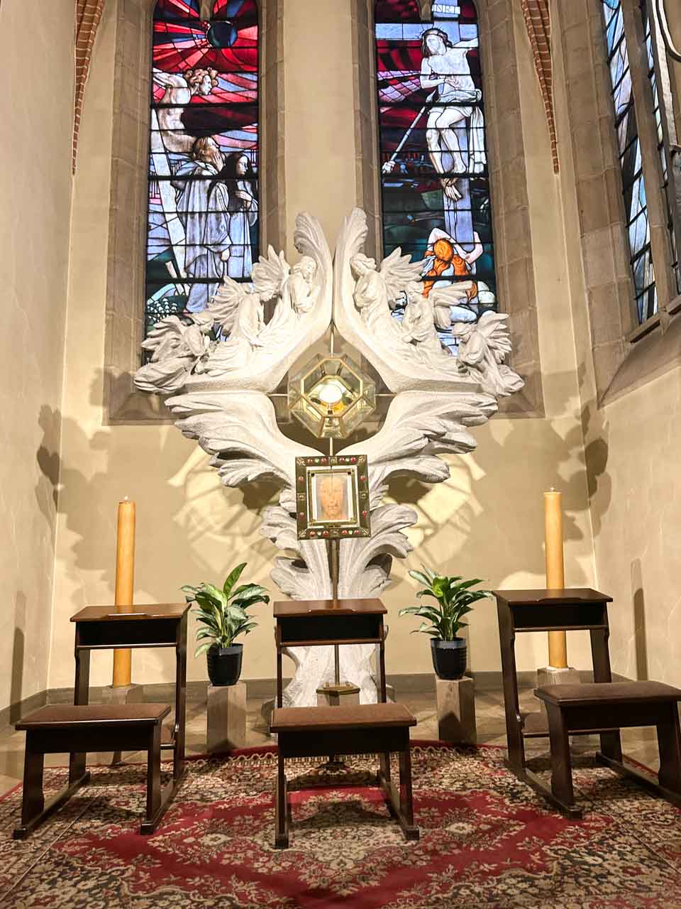 A small altar with wooden kneelers and a sculpted white backdrop, framed by stained glass windows inside the Immaculate Conception of the Blessed Virgin Mary Church in Katowice