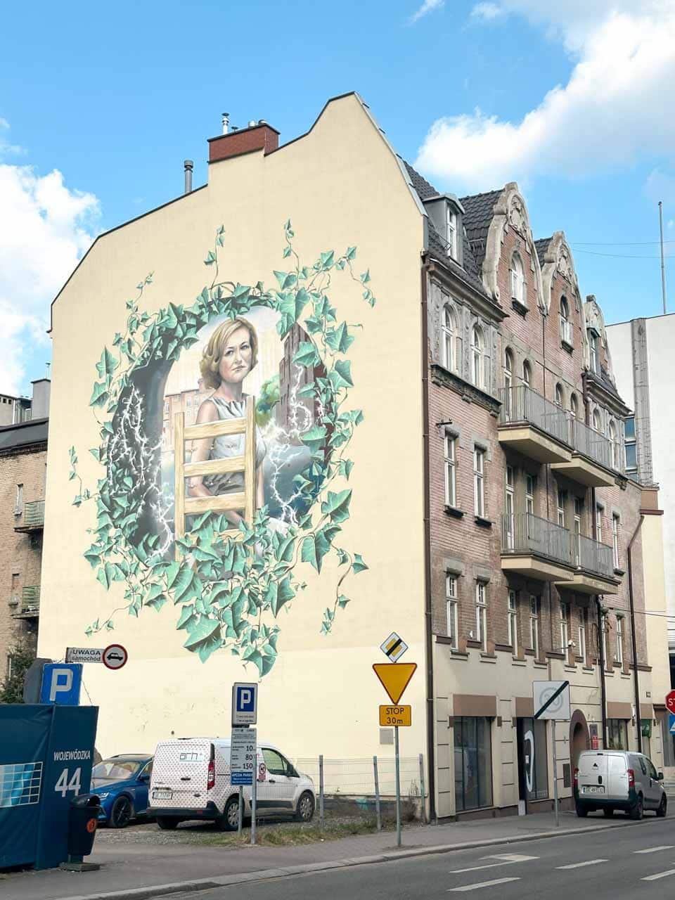 A mural of a woman framed by green ivy painted on the side of a cream building in Katowice